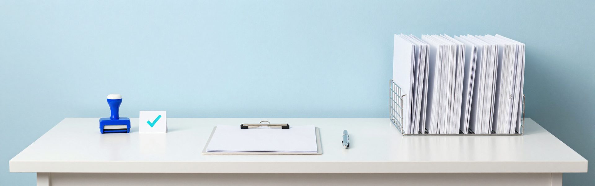 A review desk: a sign-off clipboard, an approval stamp, a card with a tick, and a tray of folders pending review